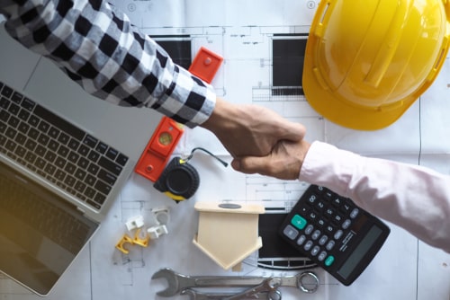 hand shake over calculator, computer, hard hat, and construction tools